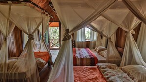 A room with four beds, each covered with a canopy. The room has wooden walls and a wooden ceiling. There is a window with a view of greenery outside. - Olympe Du Bemaraha (Bekopaka)