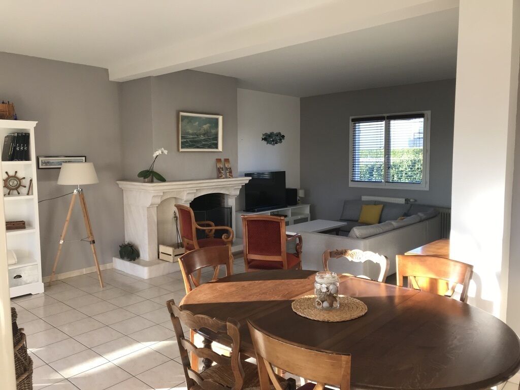 En matplats med ett runt bord och stolar, en öppen spis, en tv och ett fönster med persienner.