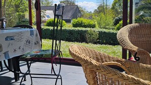 A covered patio with wicker furniture, a table with a patterned tablecloth, and a view of a house and garden. - Comfortable family home a stone's throw from the GR34 and beaches (Crozon)