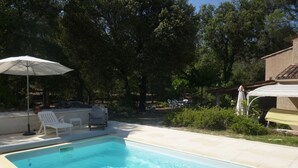 Une piscine rectangulaire à l’eau d’un bleu cristallin, entourée d’une terrasse agrémentée de chaises longues blanches et d’une table.
