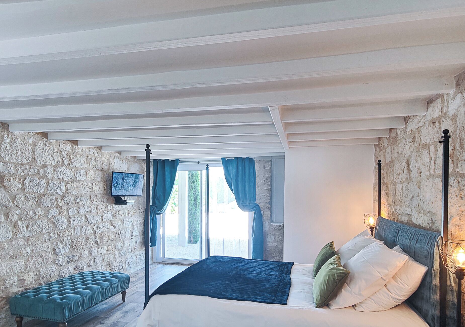 A bedroom with a bed, a bench, a TV, and a view of the outdoors.