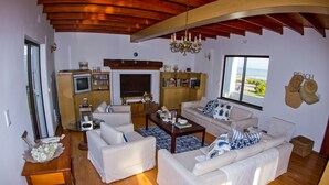 A spacious living room with a fireplace, a television, and a large window overlooking the ocean. - Storkereden (Pearly Beach)