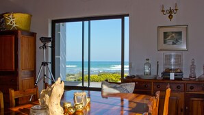 A dining area with a view of the ocean, wooden furniture, and decorative items on the table. - Storkereden (Pearly Beach)