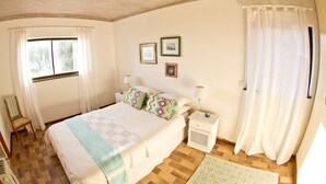 A bedroom with a bed, a chair, a nightstand, and a window with curtains. - Storkereden (Pearly Beach)
