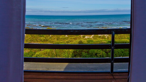 A wooden deck with a railing overlooking a coastal area with greenery and the sea. - Storkereden (Pearly Beach)