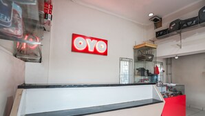 Una zona de recepción con un mostrador rojo, una vitrina de vidrio con bolsos de mano y un letrero 'OYO' en la pared.