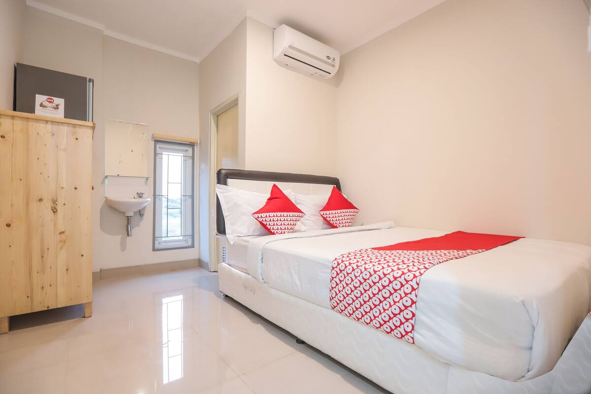 Un dormitorio con una cama, un armario de madera, un lavabo blanco y un equipo de aire acondicionado.