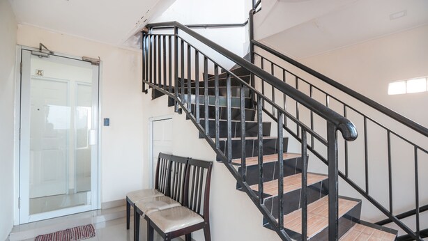 Una escalera con barandillas negras y escalones de madera, un banco y una puerta de vidrio.
