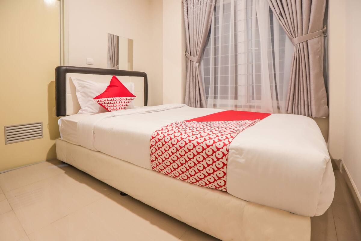 Una cama bien hecha con una colcha blanca y roja estampada, cabecera negra y una única almohada roja.