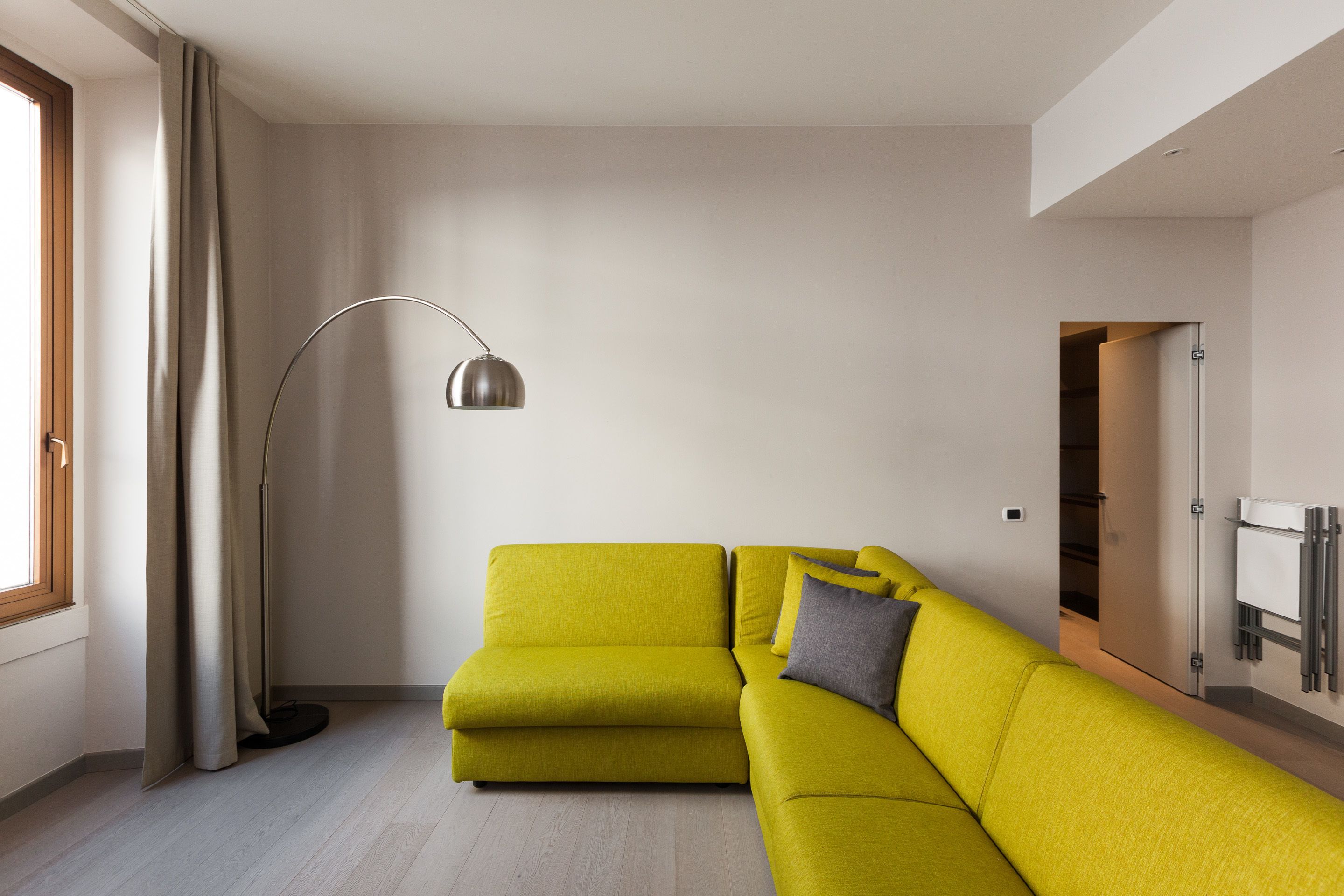 Una sala de estar moderna con un sofá amarillo, una lámpara de pie y vistas a un armario con ropa colgada.