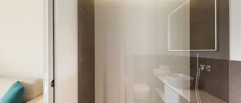 A modern bathroom with a glass shower enclosure, a white sink, and a beige sofa with a teal pillow.