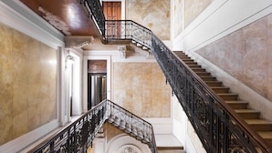 Una imponente escalera con barandillas negras ornamentadas y paredes de mármol.