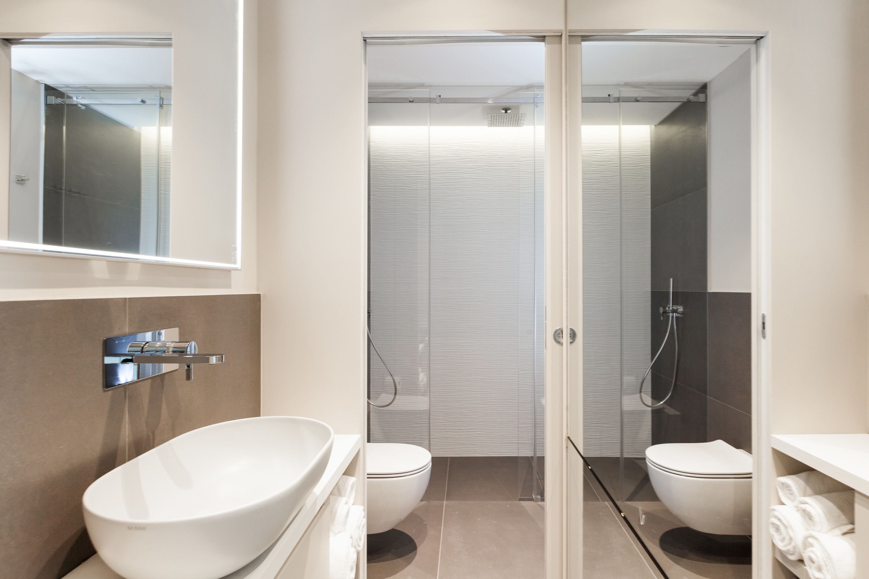 A modern bathroom with a large white sink, two toilets, and a glass-enclosed shower area.