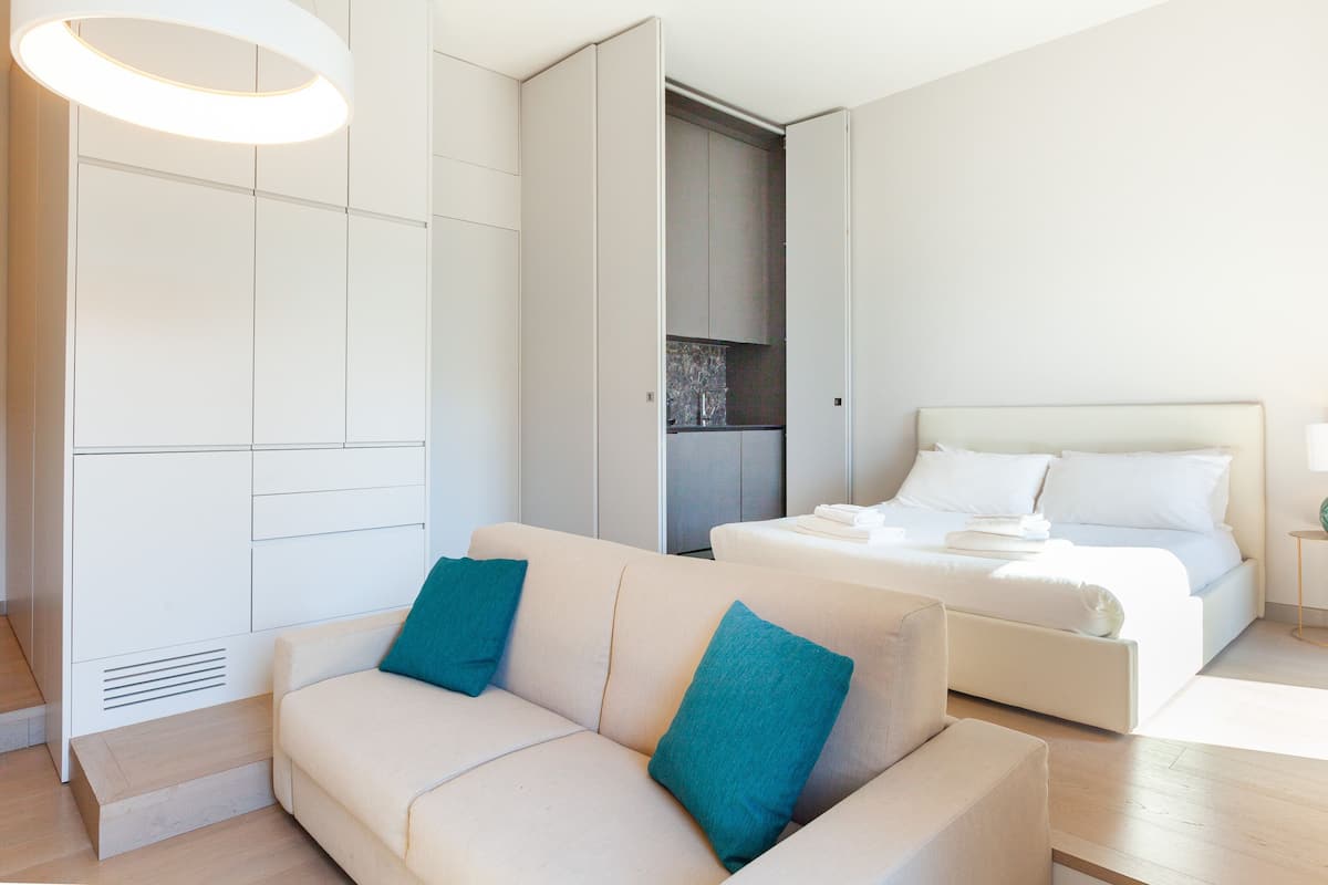 A modern hotel room with a sofa, a bed, and a built-in wardrobe.