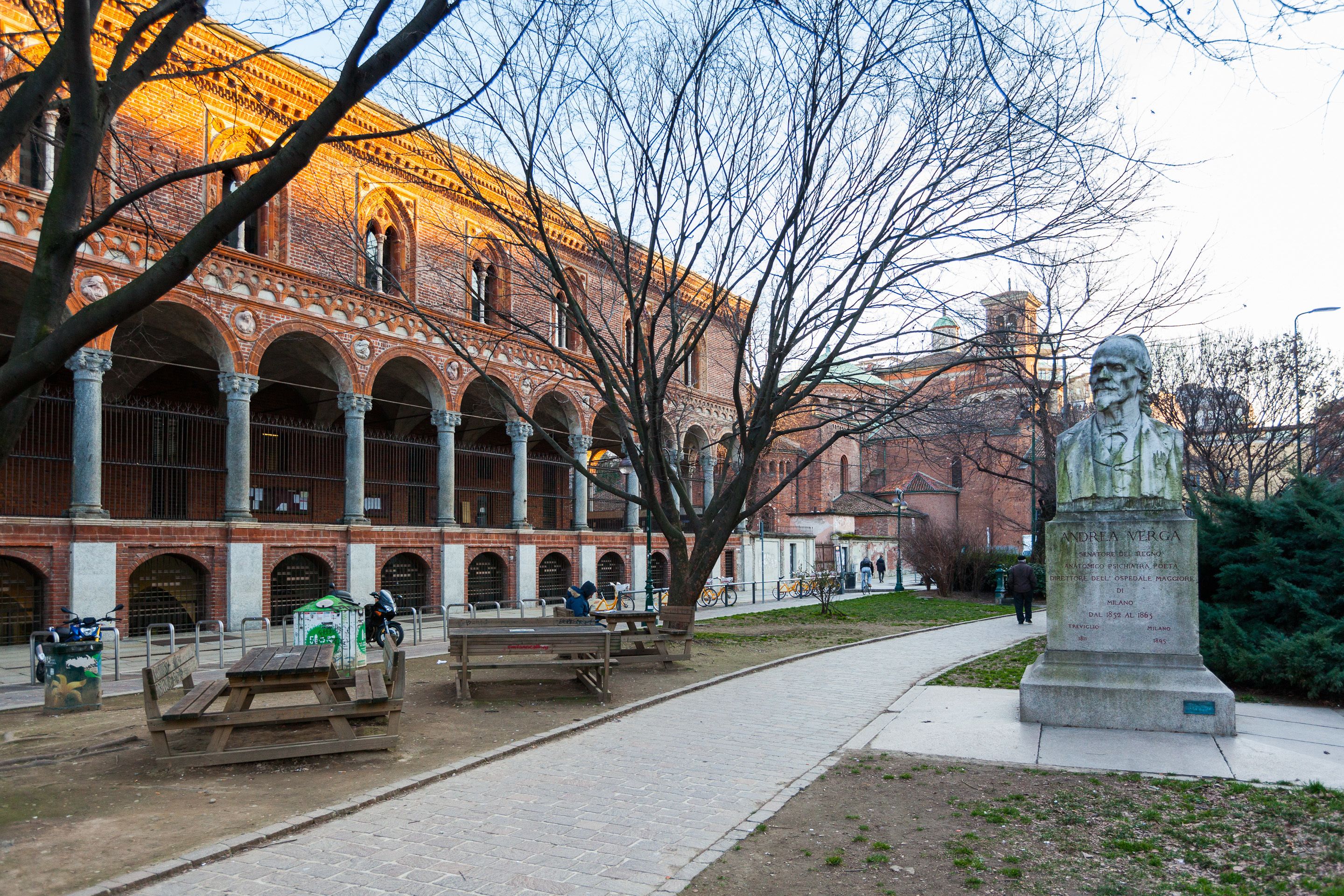 A courtyard with benches, a statue, and a historic building with arches.