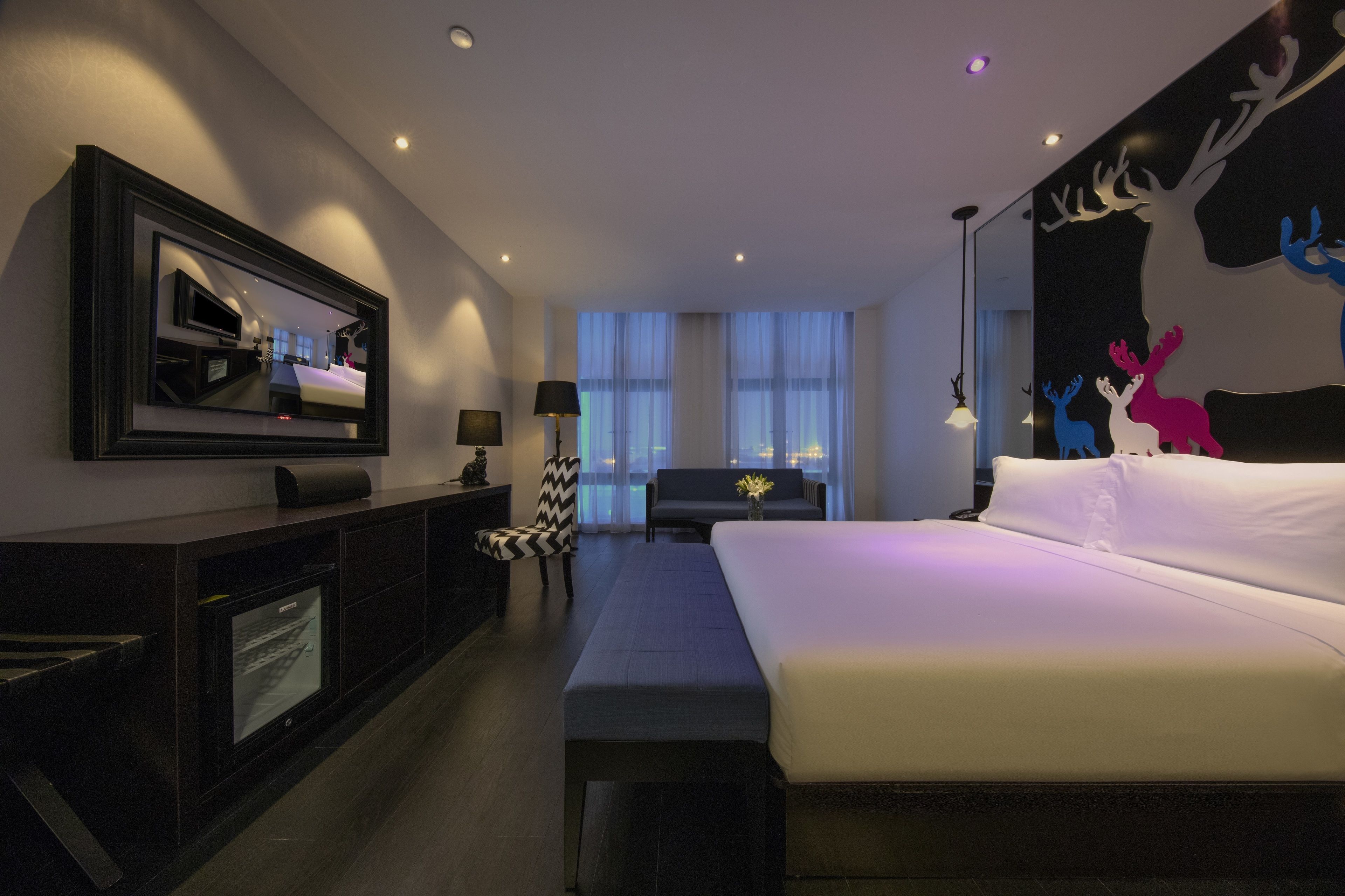 A modern hotel room with a large bed, a flat-screen TV, a desk, and a chair.