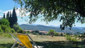 Una silla amarilla bajo un árbol con vistas a un paisaje rural con montañas al fondo.