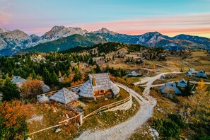 A remote mountain village with traditional houses, a dirt path, and a backdrop of rugged mountains. - Koca Ojstrica - Velika planina (Kamnik)