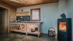 A kitchen with wooden cabinets, a stone countertop, and a wood-burning stove. - Koca Ojstrica - Velika planina (Kamnik)