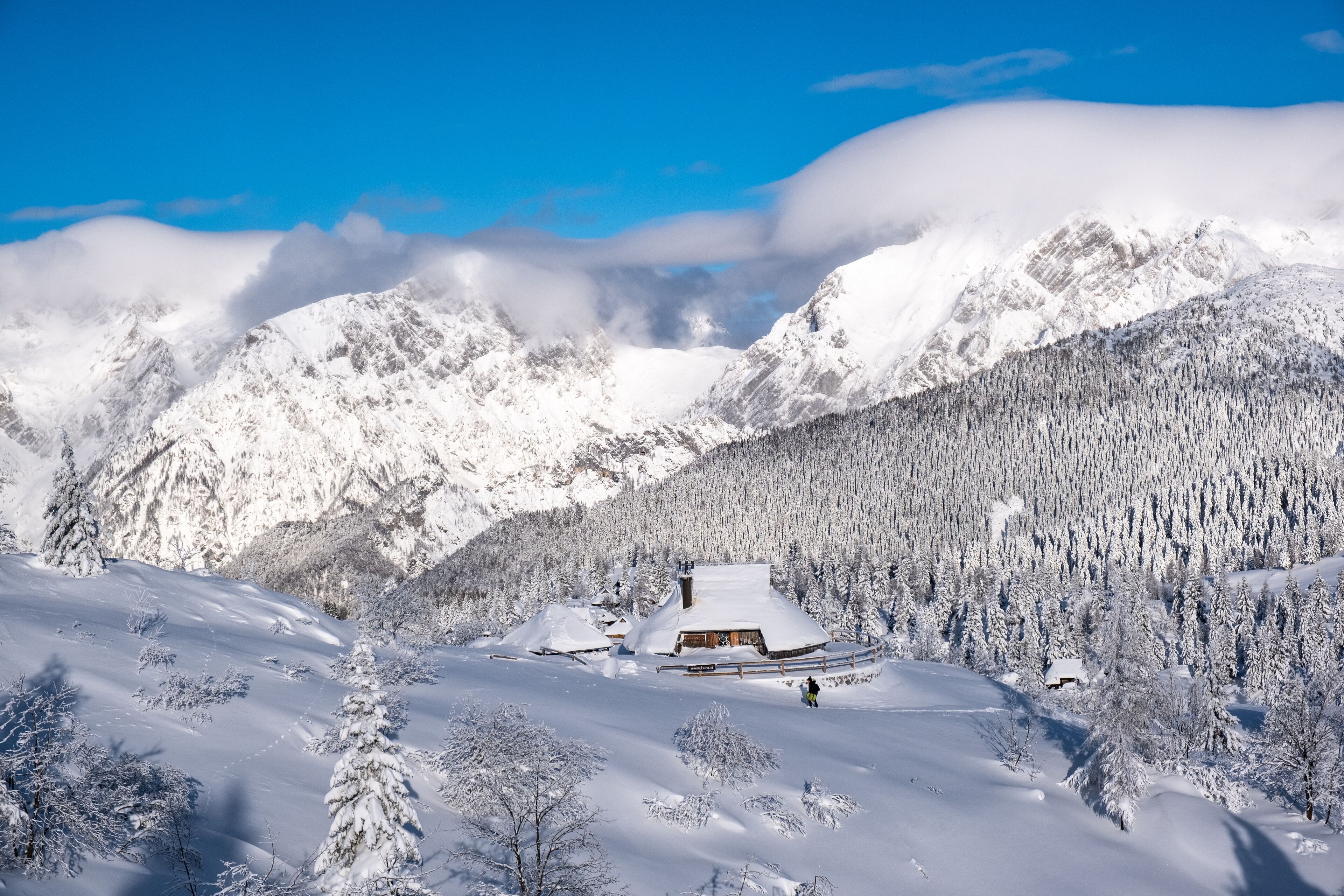 A snow-covered mountain landscape with a wooden cabin surrounded by trees.