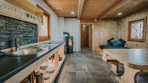 A wooden interior with a stone wall, a sink, a stove, and a bench. - Koca Ojstrica - Velika planina (Kamnik)