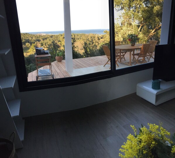 A modern interior with a large window overlooking a deck with outdoor furniture.