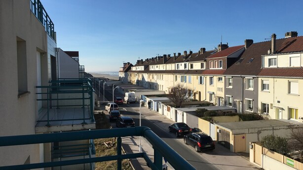 Een woonstraat met terraswoningen, een heldere lucht en geparkeerde auto's.