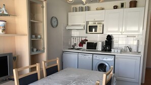 Een kleine keuken met witte kasten, een magnetron, een koffiezetapparaat en een wasmachine.