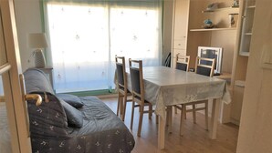 Een gezellige kamer met een bank, een eettafel en stoelen. Er is een raam met gordijnen en een lamp op een bijzettafeltje.