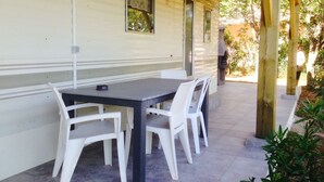 A covered outdoor area with a table and chairs, a covered walkway, and a building with windows and a door. - Mobile home in Figari at the Hamlet of San Gavino (Figari)