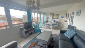 A modern living room with a TV, sofa, and dining area. - Central Arcachon T2 Apartment with Balcony & Parking, near Beach & Amenities (Arcachon)