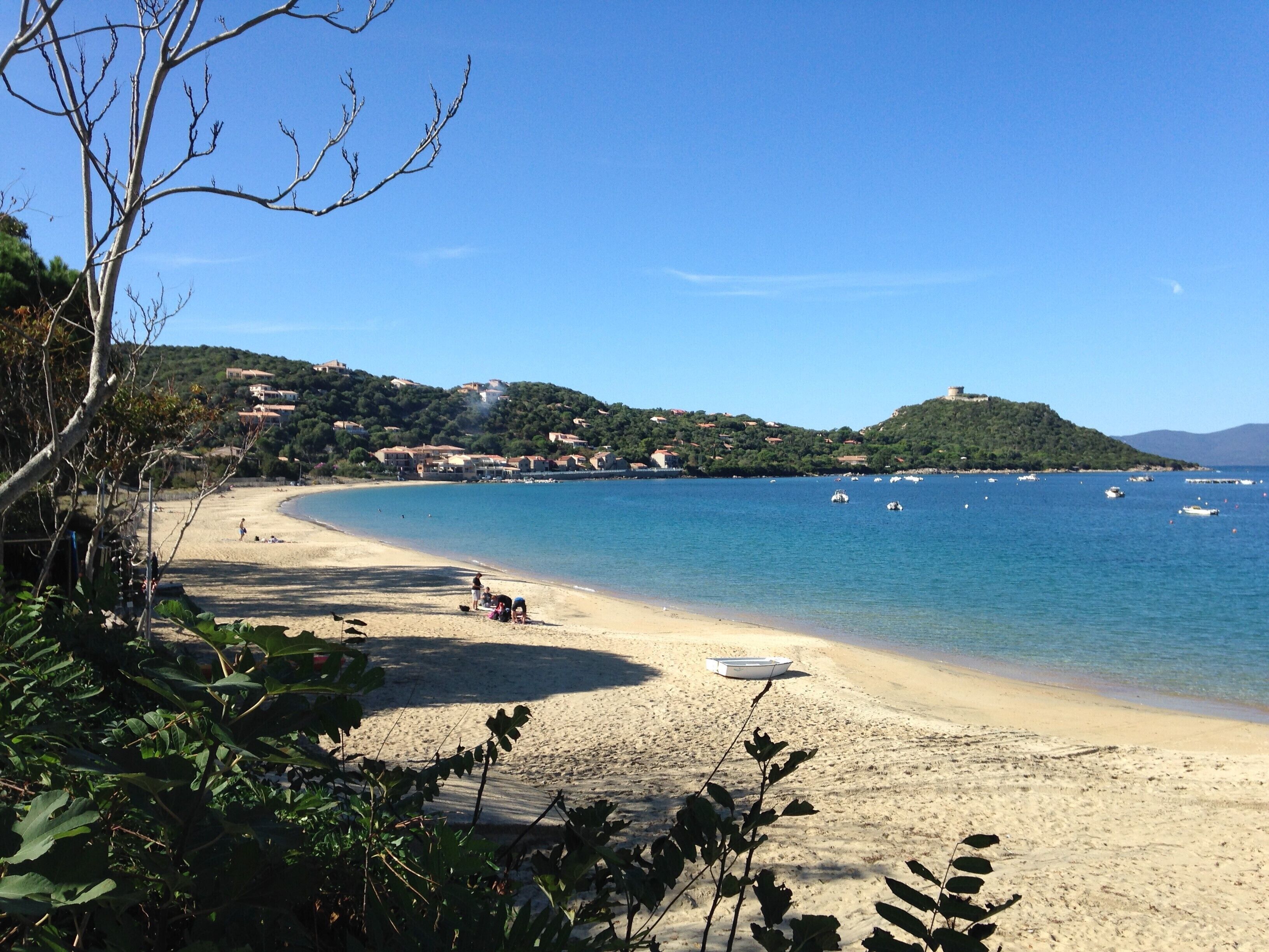 A beach with clear blue water, a sandy shore, and buildings in the background.
