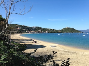 Una playa con agua azul cristalina, una orilla arenosa y edificios al fondo.