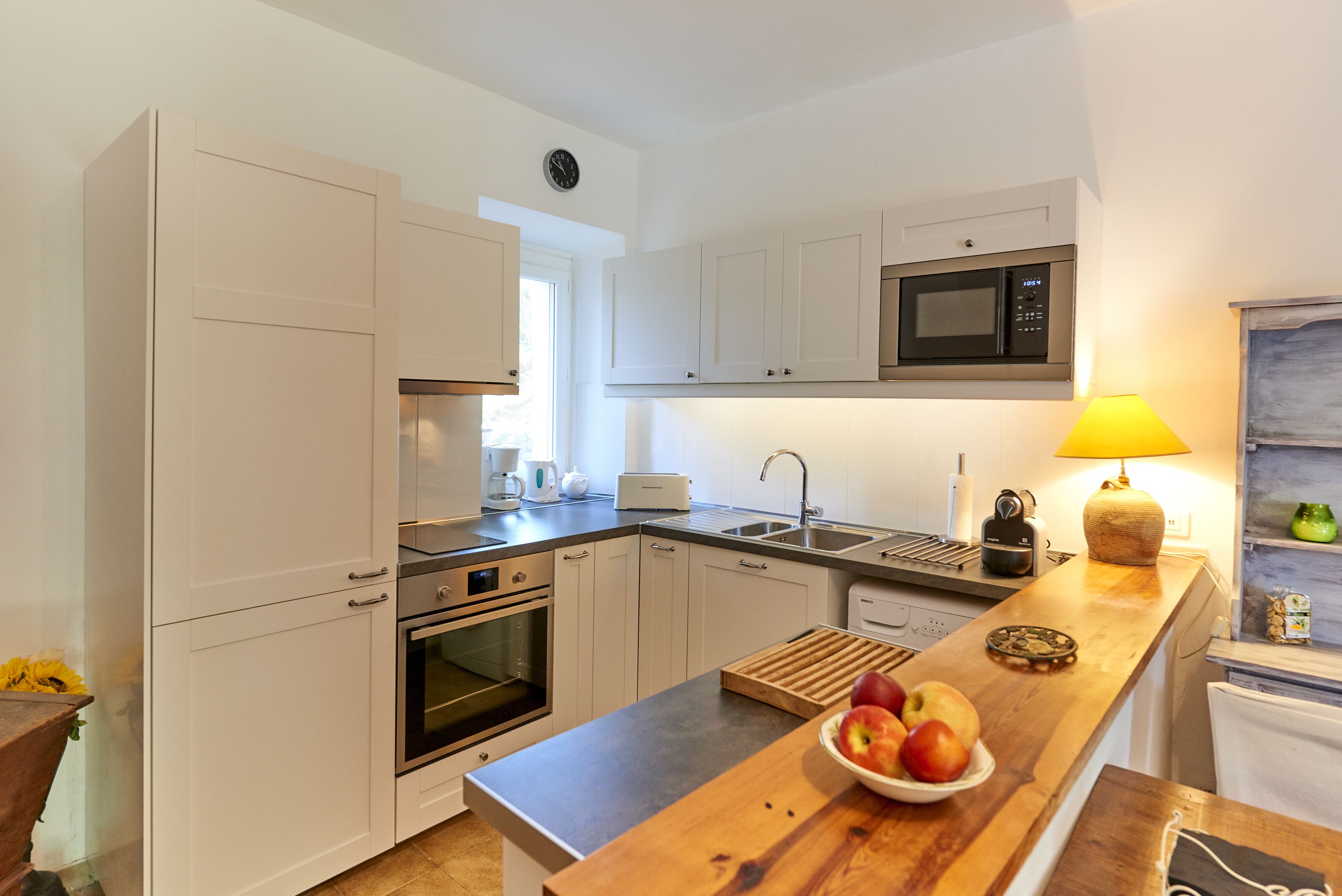 A modern kitchen with white cabinets, a microwave, a sink, and a wooden countertop with a bowl of fruit.