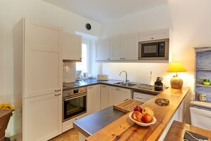 Eine moderne Küche mit weißen Schränken, einer Mikrowelle, einem Spülbecken und einer Holzausziehtafel mit Obstschale.