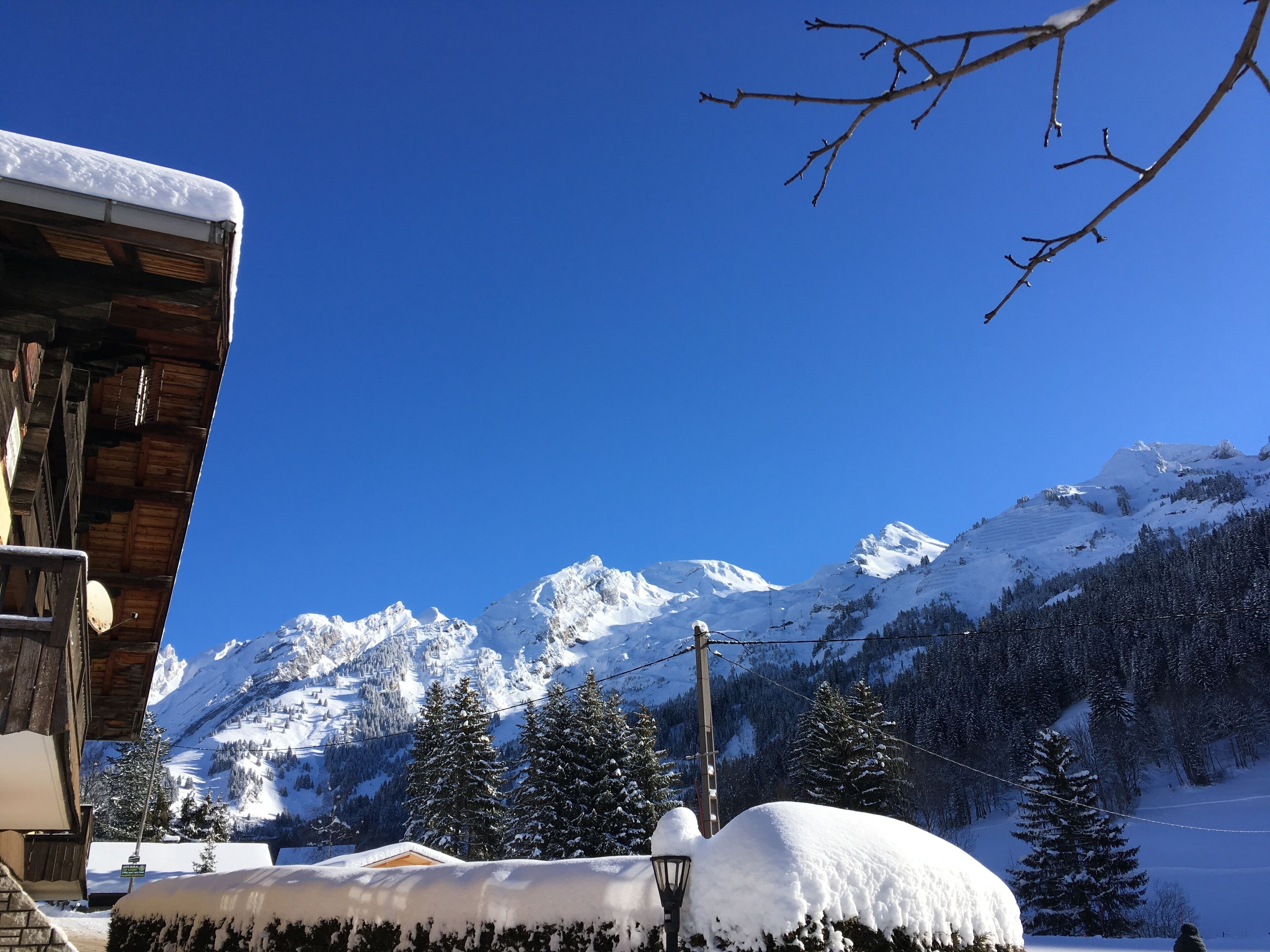 A wooden building with a snow-covered roof and a clear view of snow-covered mountains in the background.
