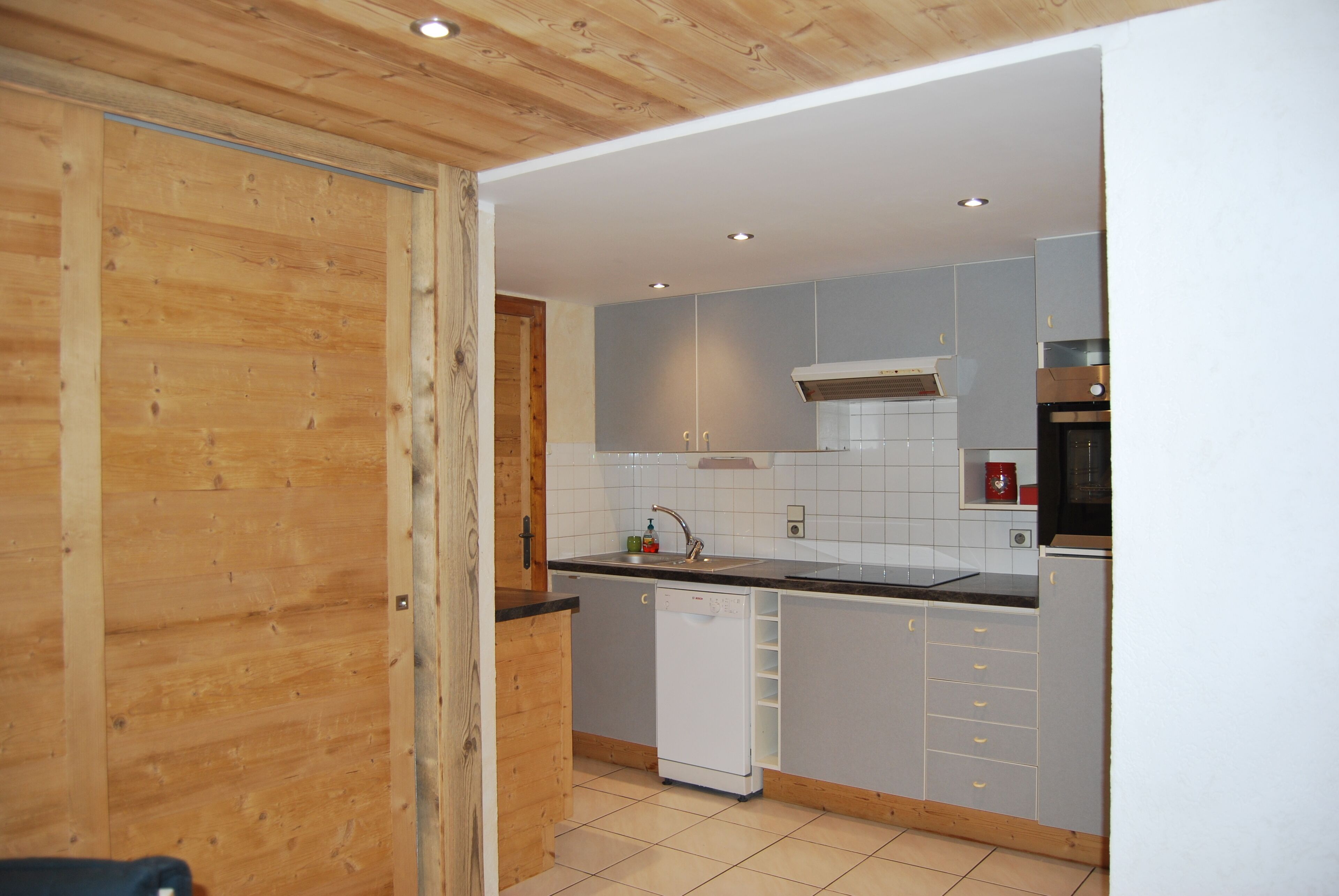 A modern kitchen with grey cabinets, a white dishwasher, and a wooden ceiling.