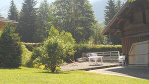Une cabane en bois avec une cour clôturée, entourée d’arbres et adossée à une montagne.