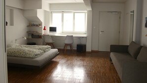 A bedroom with a bed, a desk with a computer, a window, and a door. - Basel Backpack - Hostel (Basel)