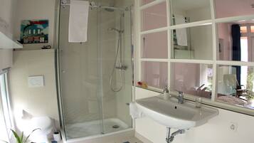 Une salle de bain avec une douche à parois de verre, un lavabo blanc et un carrelage à motifs géométriques.