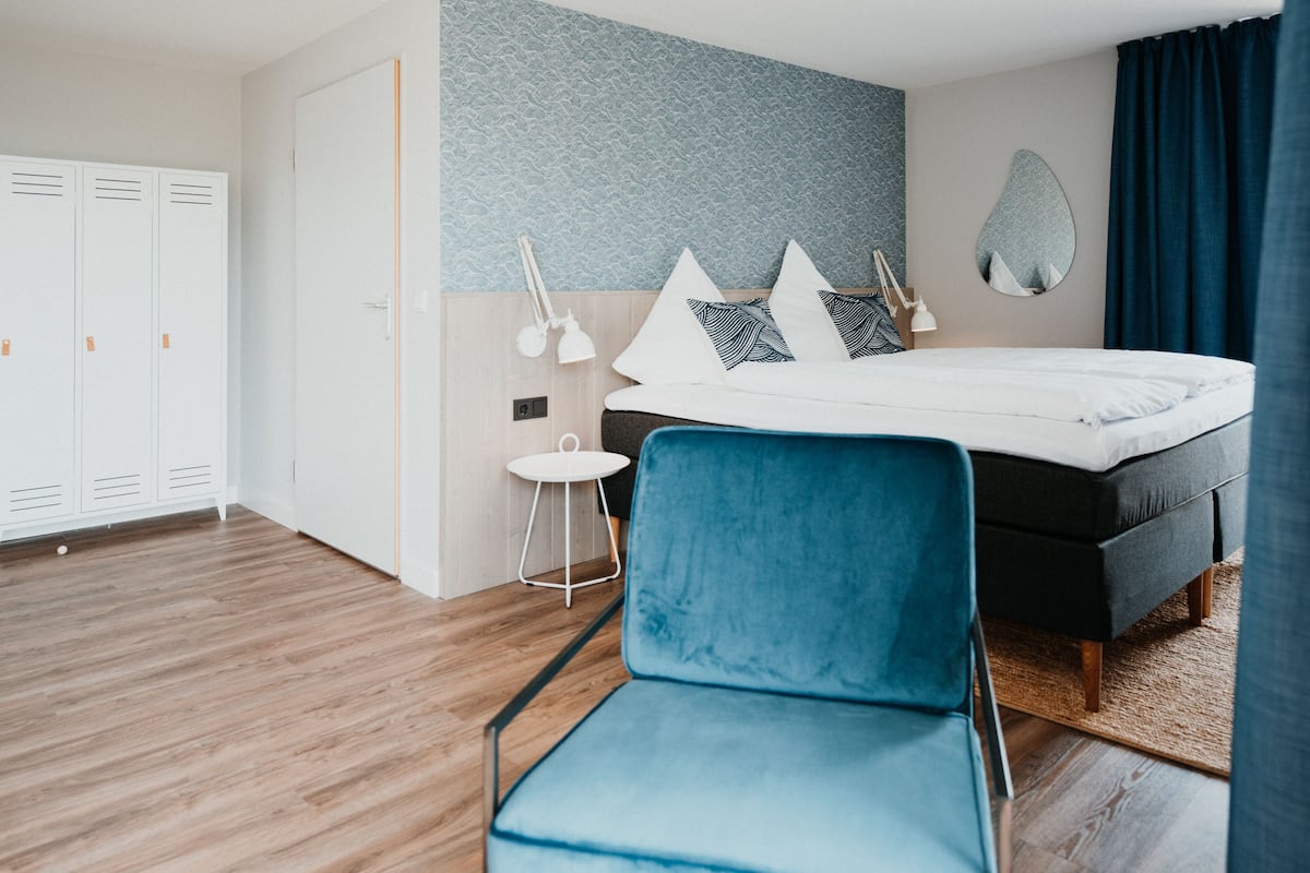 A modern bedroom with a bed, a blue chair, a wardrobe, and a small table.