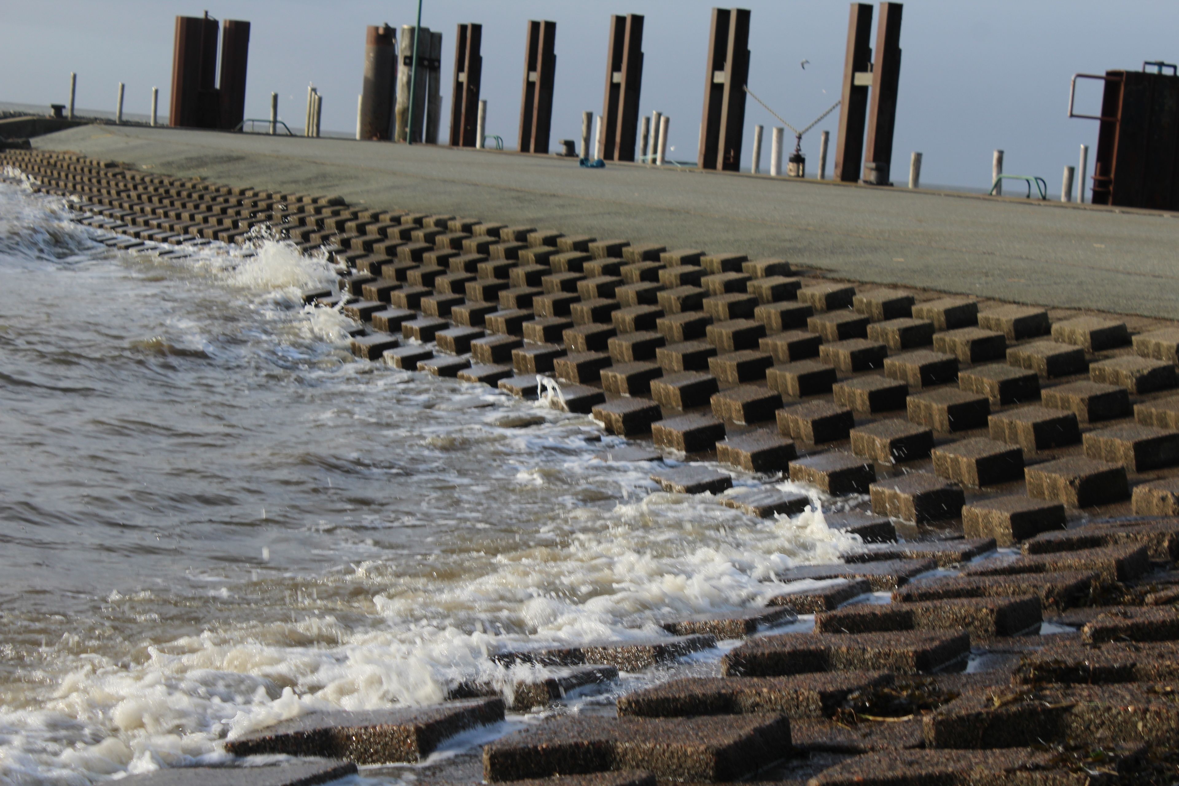 A concrete sea wall with a series of vertical pillars and a stepped design leading into the water.
