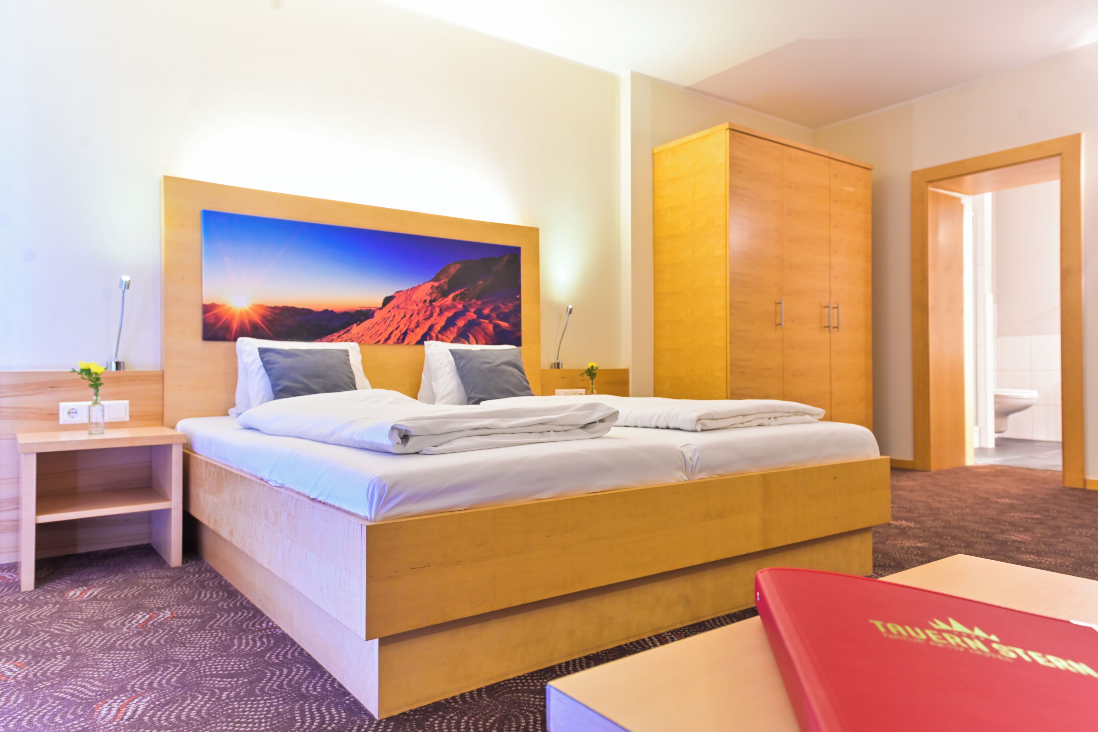 Habitación de hotel con cama, escritorio, armario y un cuadro de un atardecer.