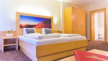 Habitación de hotel con cama, escritorio, armario y un cuadro de un atardecer.