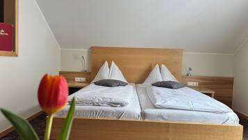 Una cama doble con cabecera de madera, dos mesitas de noche y una sola tulipán roja en primer plano.