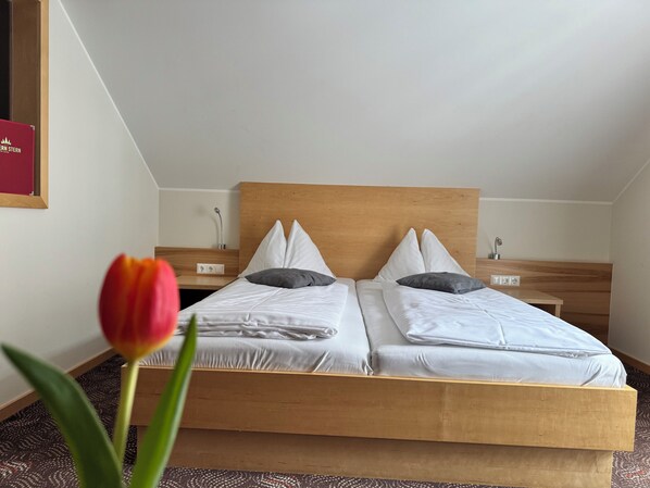 A double bed with a wooden headboard, two bedside tables, and a single red tulip in the foreground. - Hotel Tauernstern (Winklern)
