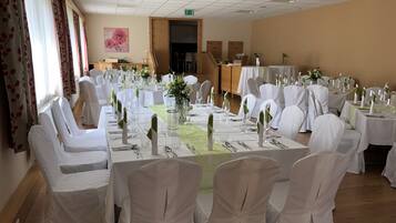 A banquet hall with round tables, white chairs, and floral centerpieces.