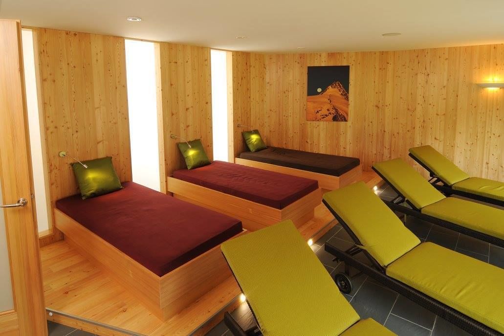 Ein Zimmer mit Holzwänden, einem Bett mit roter Matratze und einer Bank mit grüner Sitzkissen.