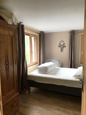 Ein Schlafzimmer mit Bett, Kleiderschrank, Traumfänger und einem Fenster mit Vorhängen.