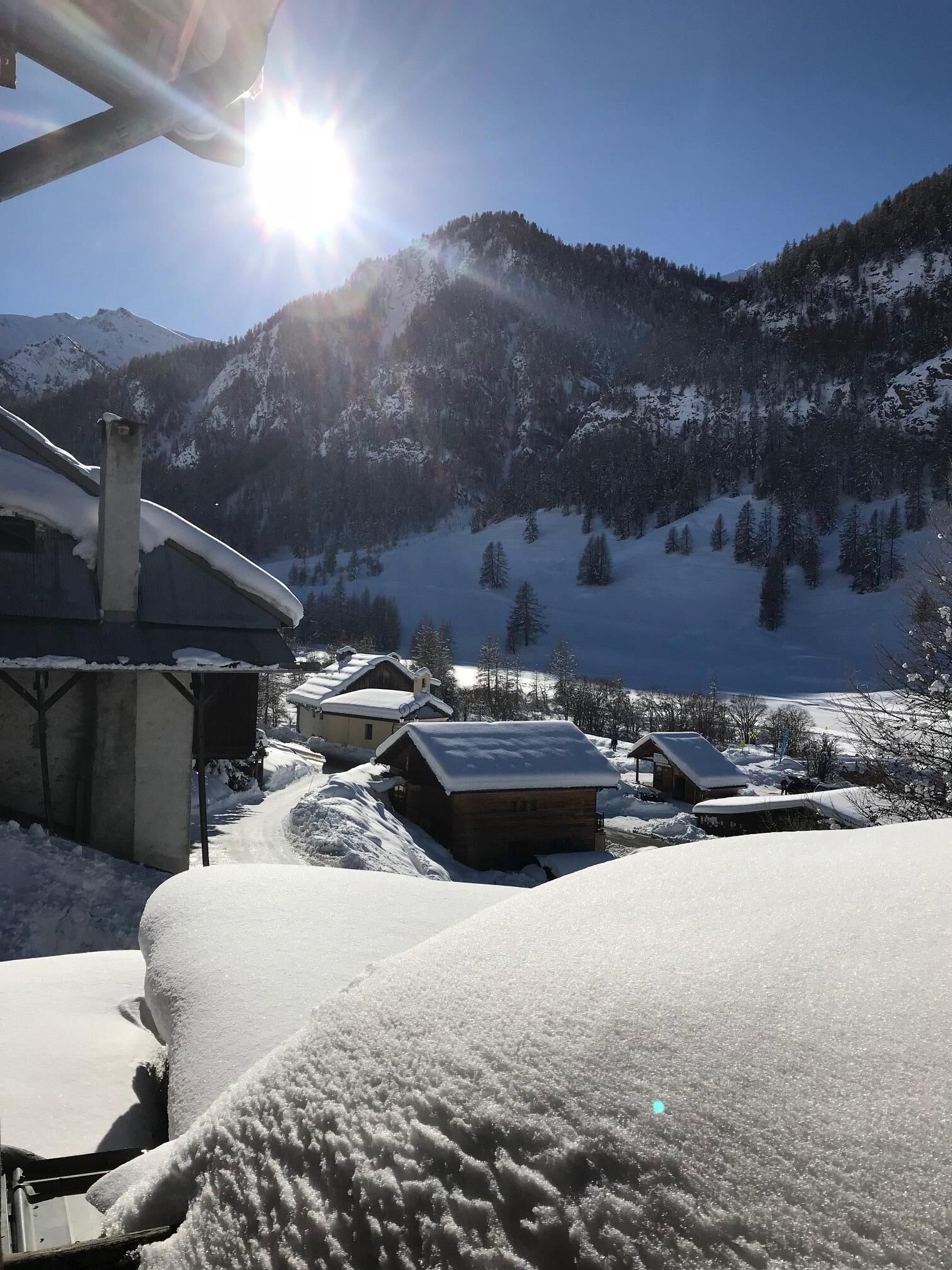 Paisatge de muntanya nevada amb cel serè, una cabana de fusta i un edifici amb teulada inclinada.